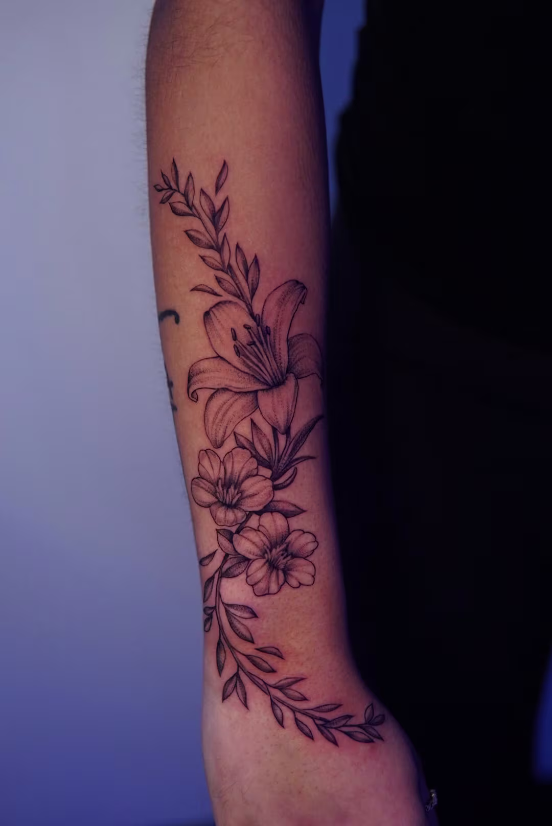 Florals (lilly and cherry blossoms) with leaves on the top of the right forearm.