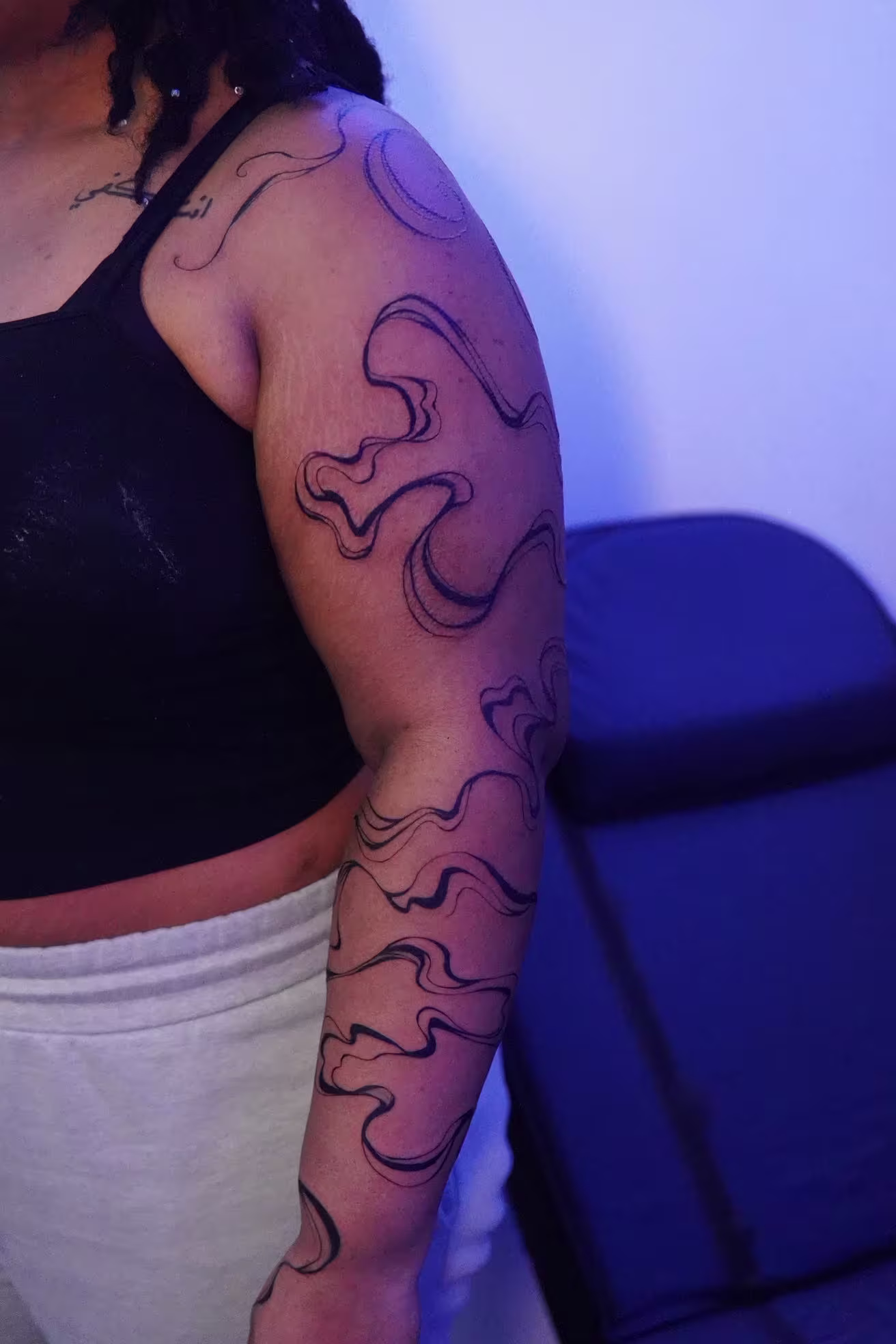 Flowy/smoke-like linework from the top of the shoulder wrapping around the arm down to the thumb.